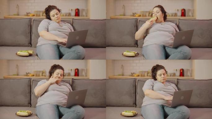 懒惰的肥胖女性脸上有番茄酱吃三明治，在笔记本电脑上输入信息