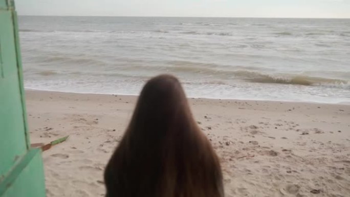 悲伤的沉思的混合民族妇女走下楼梯到沙滩，转身，看着镜头离开。风吹动体贴女性的长发。海浪在海边。