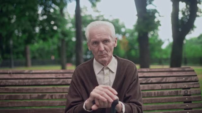 沮丧的皱纹老人独自坐在城市公园里，拿着拐杖