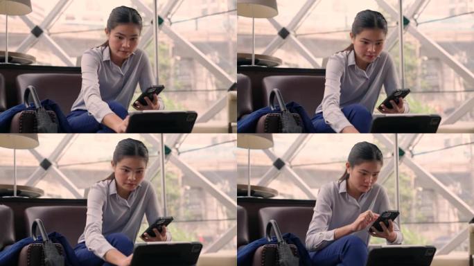 坐在咖啡馆里的亚洲女人。她在咖啡店内使用手机和平板电脑在现场工作。