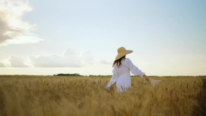 年轻女子正在享受成熟麦田的美丽，在耳朵之间旋转，穿着白色连衣裙的快乐女士