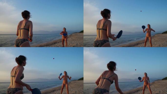 两个女人在美丽炎热的夏夜在海滩上享受桨网球