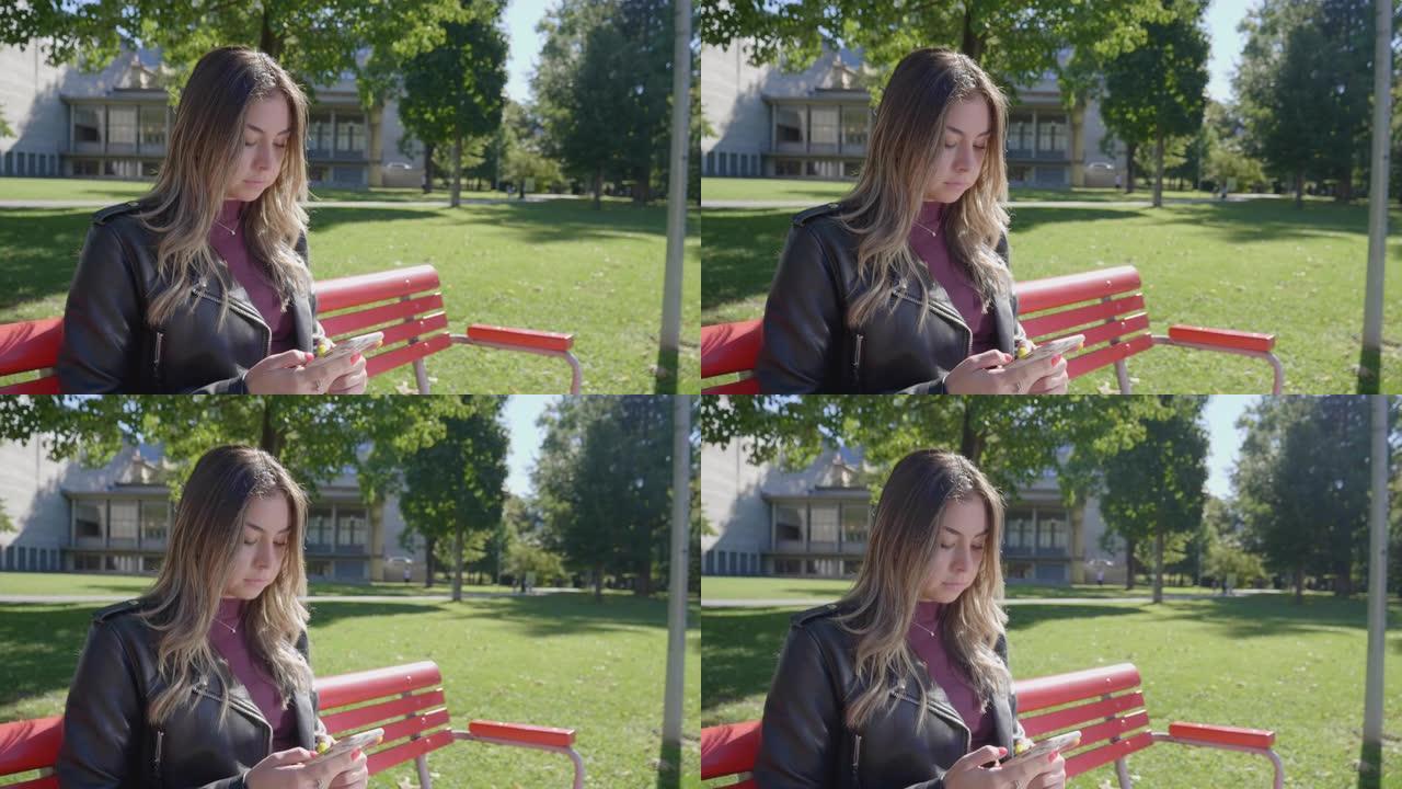 坐在公园长椅上的年轻女子使用手机发短信