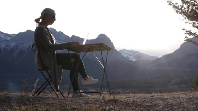女人用笔记本电脑在野餐桌上放松，远处的山脉