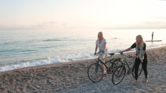 两名高级妇女沿着海滩推自行车