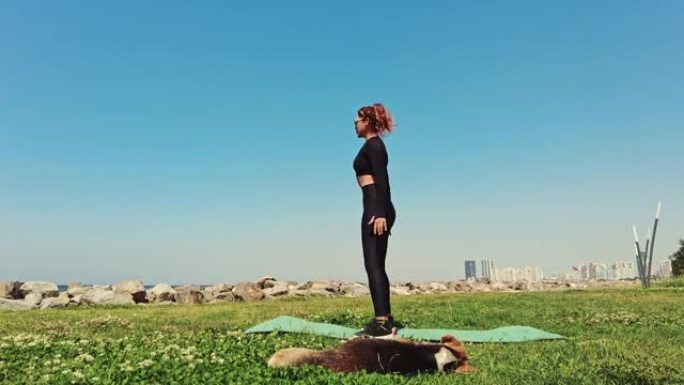 年轻女性在绿色草地上的海边用瑜伽垫锻炼