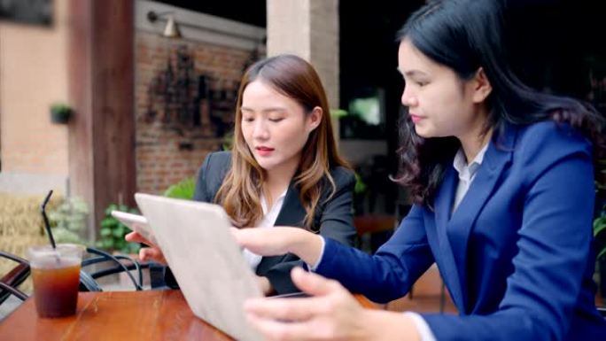 两名亚洲商务女性穿着礼貌的西装开会认真谈论咖啡馆外的工作。