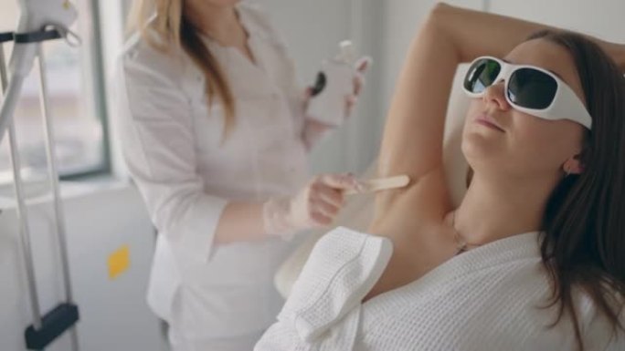 成年女性在临床上进行现代激光脱毛治疗时，美容师正在腋下皮肤中使用凝胶