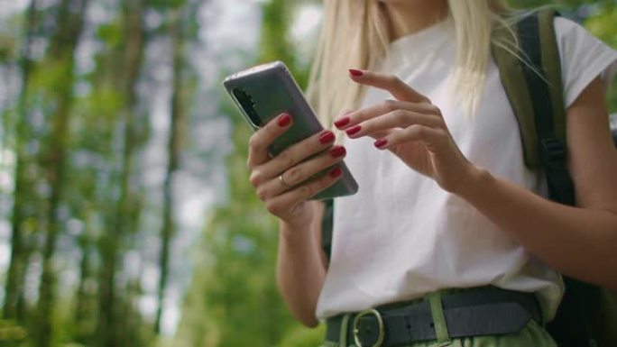 一个走过森林的女旅行者手中的手机特写。社交网络导航器和信使。用手机在树林里散步
