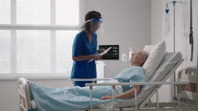 一名黑人女外科医生正在和一名躺在病床上的老年男性患者交谈。一名女性心脏病专家传染病专家正在诊所与患者