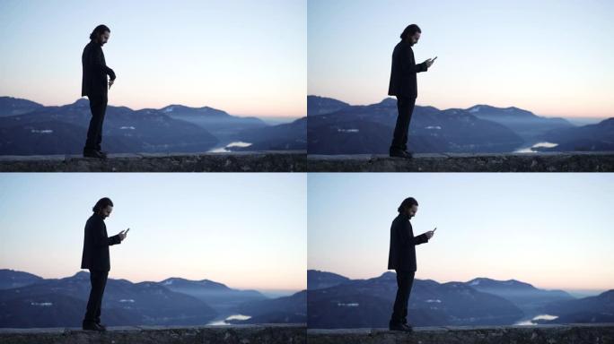 商人使用智能手机，日落光站在湖泊和山脉的视线上