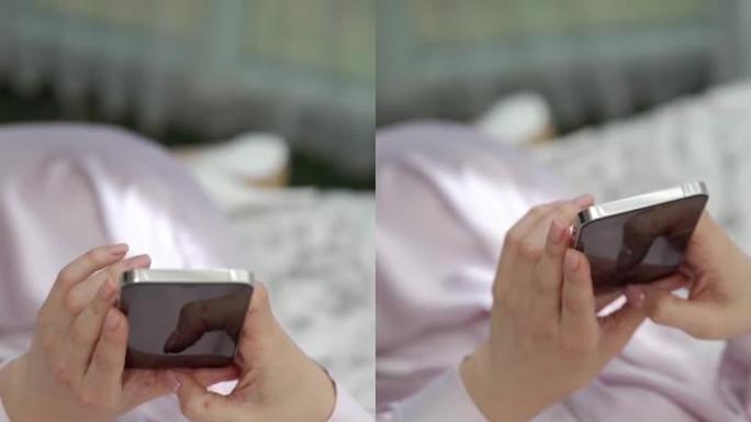 垂直夹。一位穿着粉色睡袍的优雅女子躺在床上，看着手机。