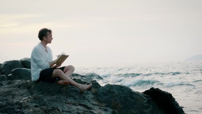 一名男子坐在海洋附近的岩石上写书的特写镜头
