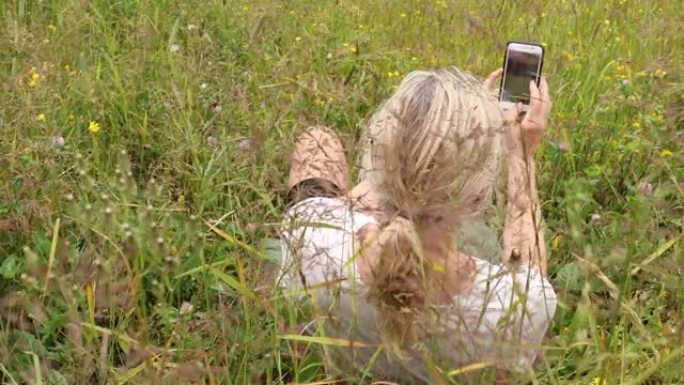 成熟的女人用智能手机在草丛中放松