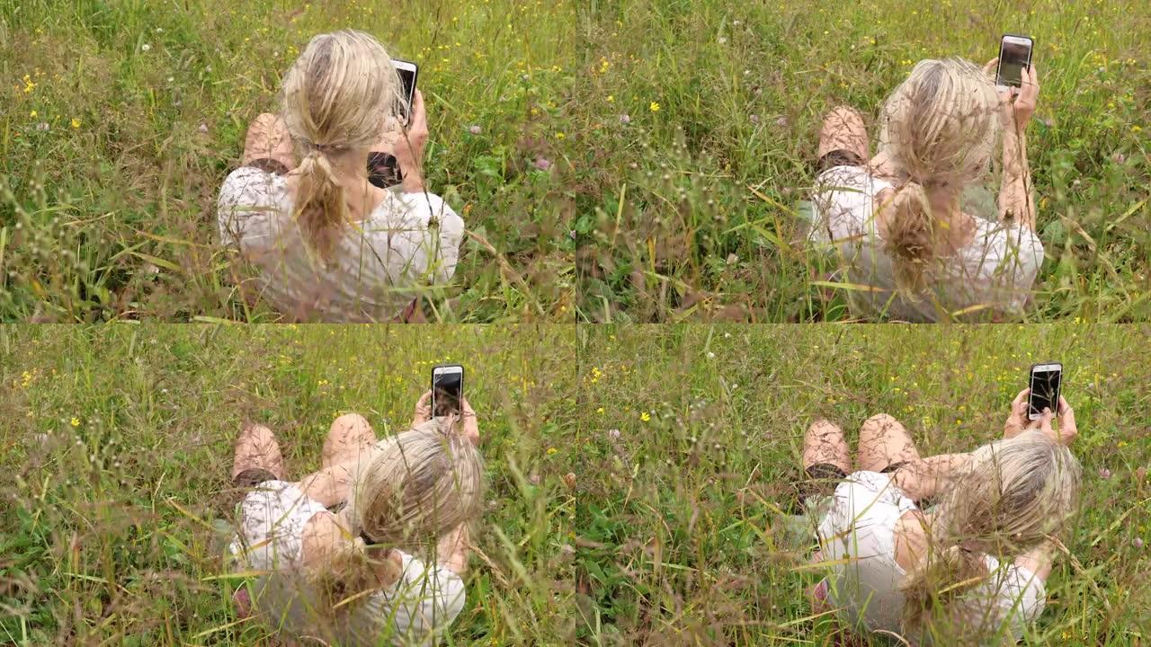 成熟的女人用智能手机在草丛中放松