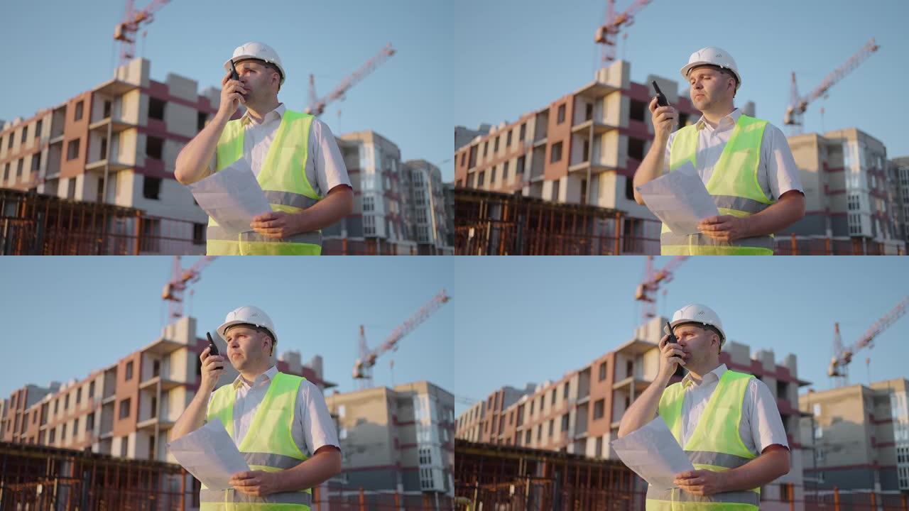 头戴头盔和背心的工头与建筑商在对讲机上交谈，站在建筑工地，跟踪镜头。建筑专家工程师用收音机和一些建筑