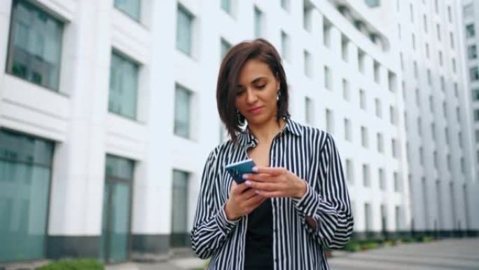 有魅力的女人在智能手机上输入短信，城市景观中成功女士的肖像