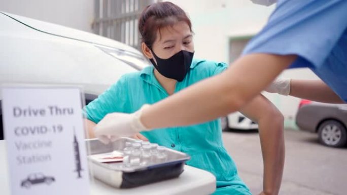 开车经过疫苗接种站，年轻的亚洲医生为那些驾驶私人汽车到站的人注射新型冠状病毒肺炎疫苗。