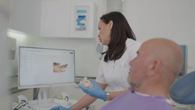 高加索女牙医，在计算机上向患者显示牙齿的3D扫描