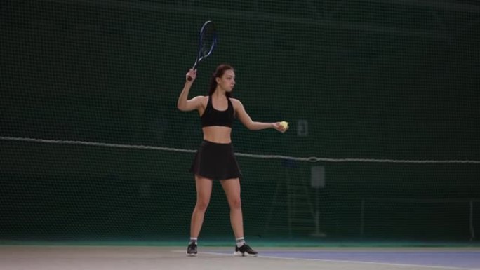 年轻苗条的女子穿着网球运动服在球场上扔球并发球，全身肖像在室内射击