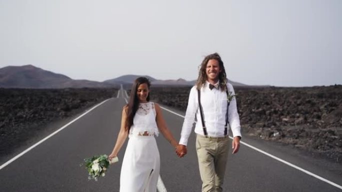 新婚新娘和新郎在火山岛上的一条空旷的道路上行走的特写镜头，背后是群山