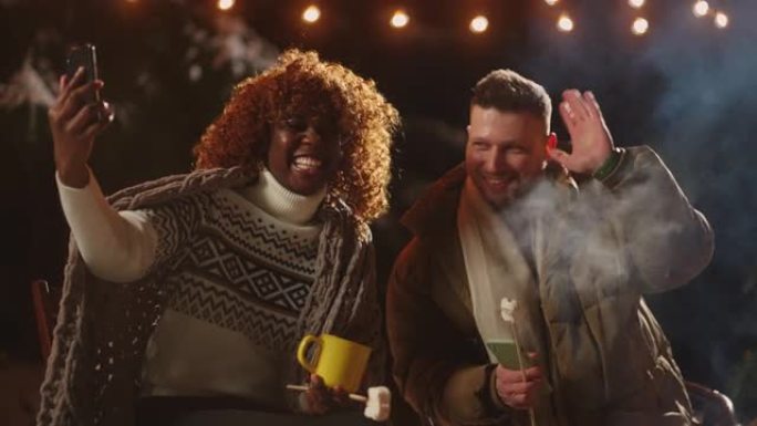 快乐的非洲妇女和她的欧洲男友在圣诞节之夜通过手机通过视频打电话