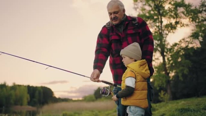 男孩在湖里钓鱼，祖父或爸爸在帮助他，幸福的家庭在大自然中休息