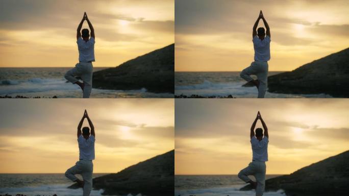 祈祷姿势的男人在海滩做瑜伽。美丽的日落