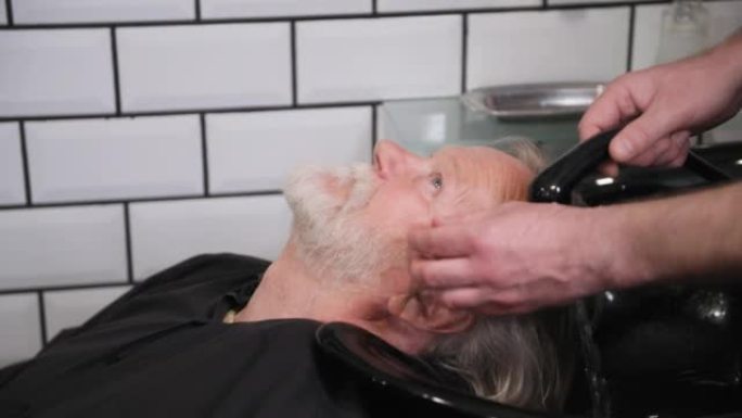 男士沙龙，一名男理发师在理发店的水槽里为一位老人在专业的椅子上洗头