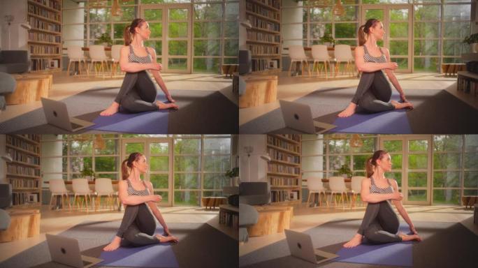 女运动员用笔记本电脑在瑜伽垫上做脊柱扭转。放松的家庭锻炼