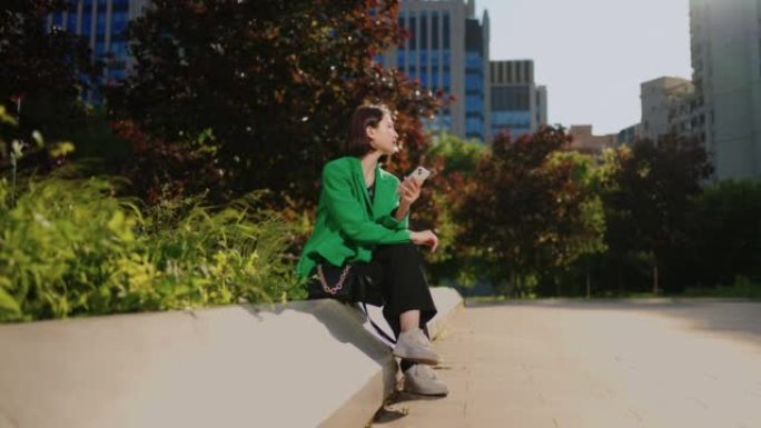 韩国年轻女子独自坐在市中心的广场上使用手机，上网成瘾
