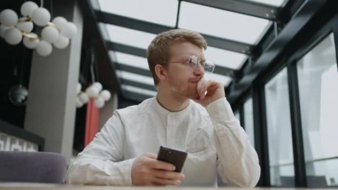 一个戴着眼镜的年轻人，手里拿着手机，看着屏幕，打印出一条信息。戴着圆形眼镜的潮人在手机上写了一条消息