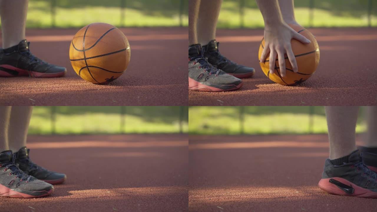 篮球球的特写镜头躺在户外球场的阳光下，因为无法辨认的球员拿起运动器材离开。积极生活方式和体育游戏的概