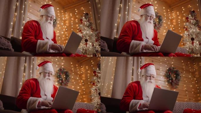 圣诞老人正在家里的电脑上工作，在装饰好的圣诞树背景下的神奇圣诞灯中