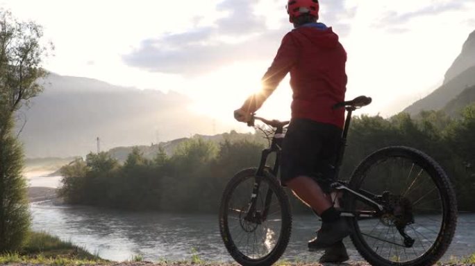 男性骑自行车的人在黎明时沿着山河上方的轨道前进