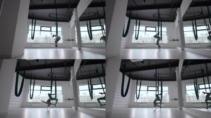 有吸引力的健身教练在绿色吊床上做反重力空中瑜伽练习。年轻灵活的女性在健身俱乐部练习航空伸展秋千。女性