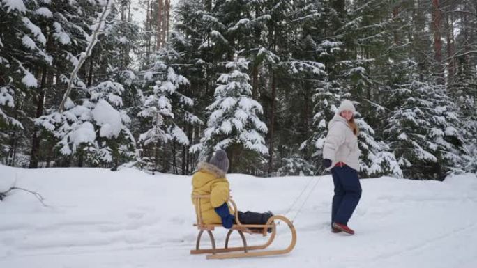 快乐的女人和她的小儿子在森林里玩得开心，母亲带着孩子拉雪橇