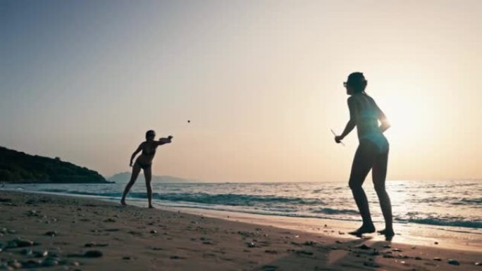 两个女人在美丽炎热的夏夜在海滩上享受桨网球