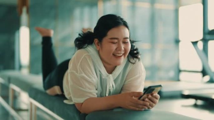 积极的亚洲女性在健身房使用智能手机时大笑