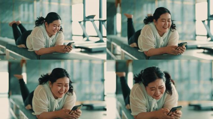 积极的亚洲女性在健身房使用智能手机时大笑