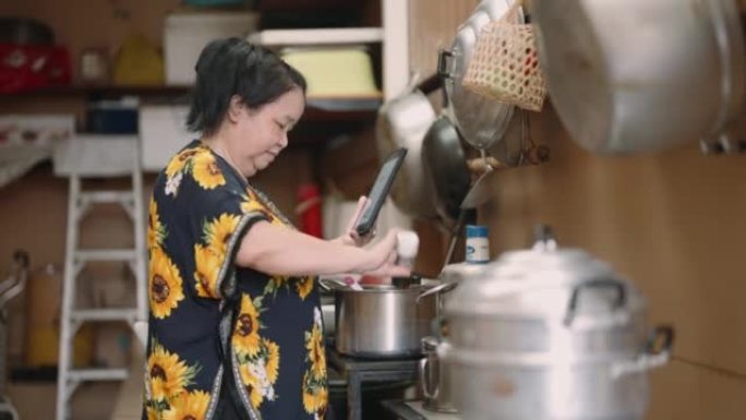 亚洲高级女性在家准备食物并检查平板电脑上的食谱或视频教程
