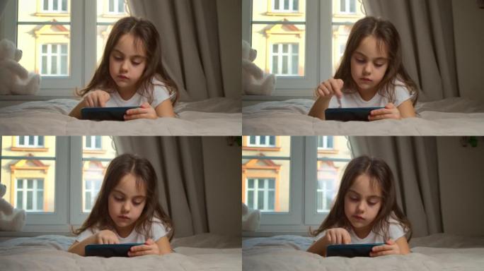 可爱的小女孩拿着智能手机在家欣赏手机电影。小孩子正在用手机学习，观看视频，享受移动技术的概念。