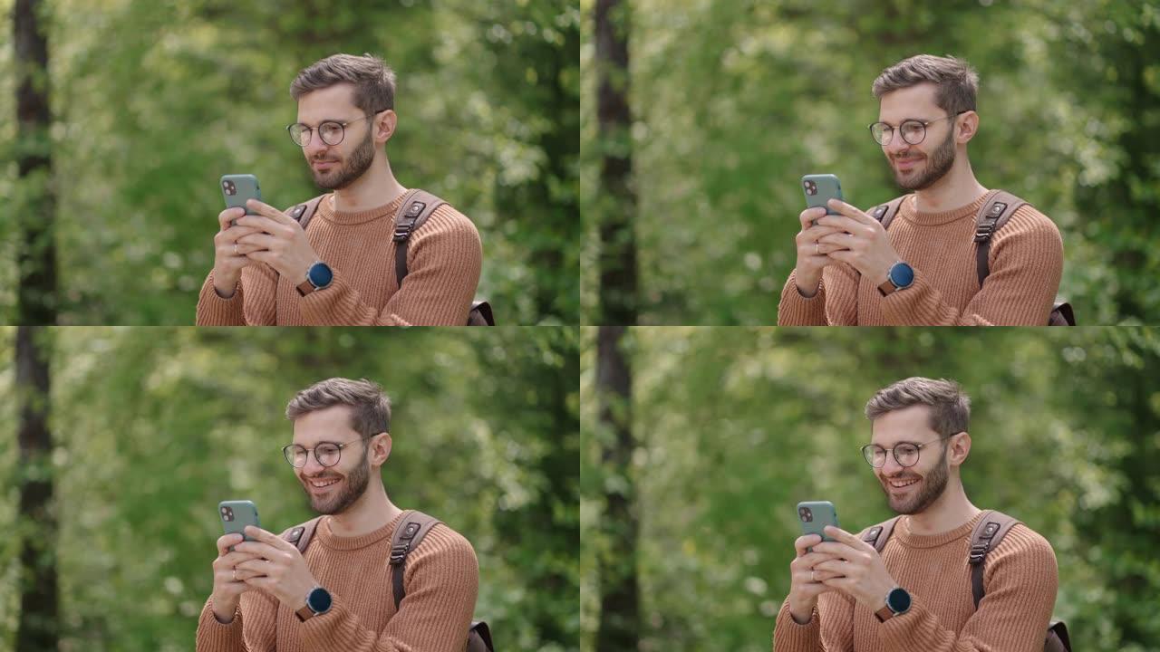 一个年轻人在树林里背着背包，在大自然中用手机写信息。在空旷地区的游客在聊天中交流，看照片，高兴，微笑