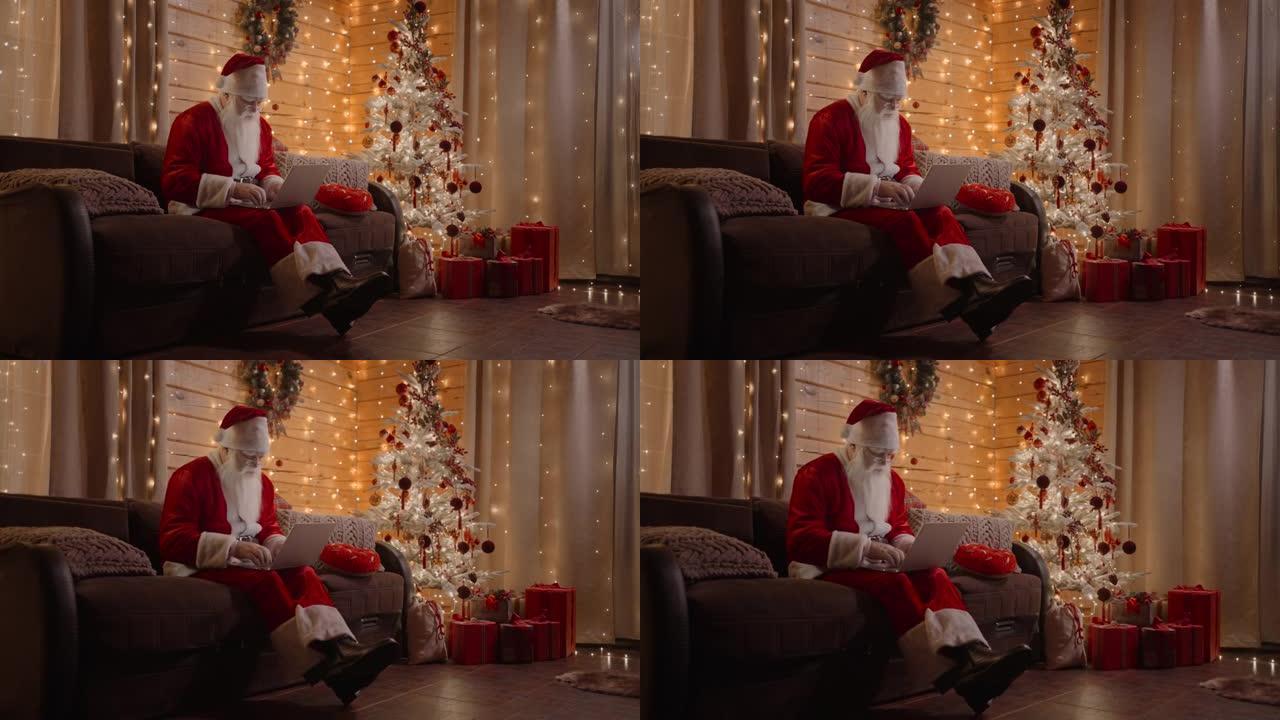 圣诞老人正在家里的电脑上工作，戴着眼镜和胡须，在圣诞节前夕，装饰好的圣诞树的背景上有神奇的圣诞灯