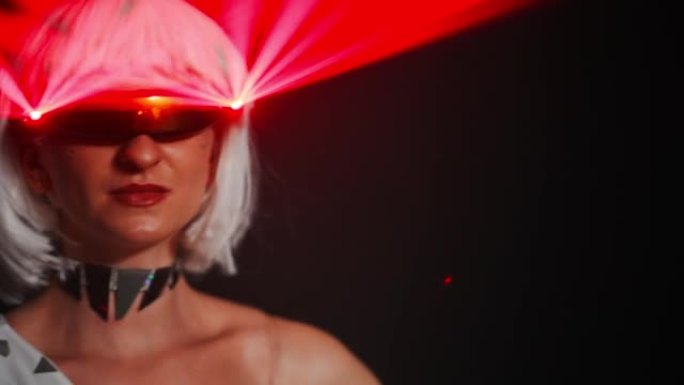 戴眼镜的自信女人的头像照片，红色激光转动头站在黑色背景下。白人女性表演者在黑暗中的舞台上的特写镜头。