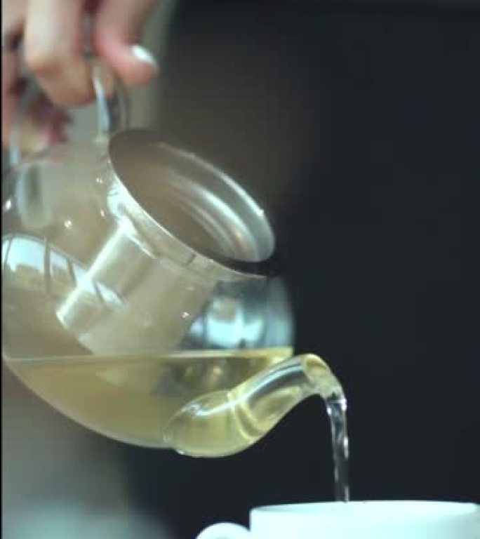 女性手捧壶将茶倒入杯子的特写镜头