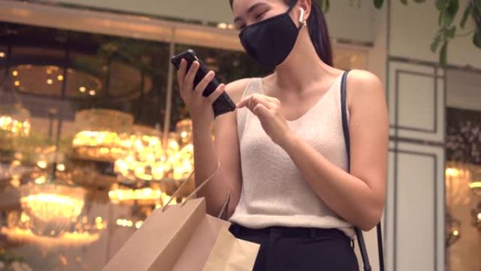 亚洲妇女在购物中心大楼外购物时在面具后面微笑