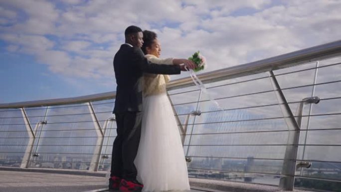 快乐浪漫的新婚夫妇在慢动作中模仿泰坦尼克号的场景，站在桥上欣赏户外风景。阳光明媚的日子，微笑着慈爱的