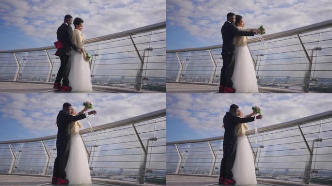 快乐浪漫的新婚夫妇在慢动作中模仿泰坦尼克号的场景，站在桥上欣赏户外风景。阳光明媚的日子，微笑着慈爱的