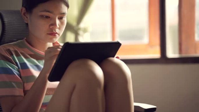 亚洲妇女坐在符合人体工程学的椅子和数字笔在平板电脑上画画。